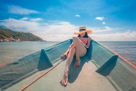 slim woman relax and enjoy the sea by sitting lie down on prow of the local ferry boat bow, holiday and long weekend vacation traveling in summer timeの写真素材