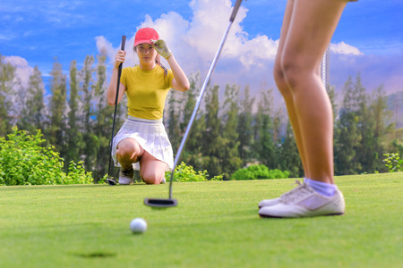 Young woman golf player looking to golfmate competitor putting golf ball to the hole on green with exciting emotionの写真素材
