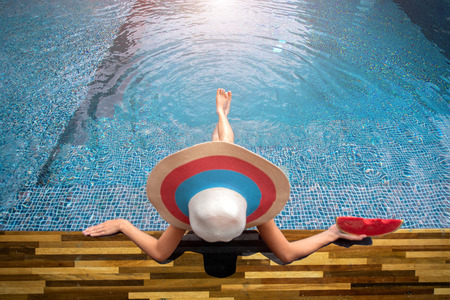 legs of woman paddle water in the pool, sitting at edge of swimming pool, enjoy and relax happiness...