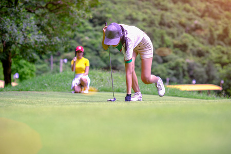 legs of woman golf player step-in to takes golf ball from the hole on the green, golfmate competitor...
