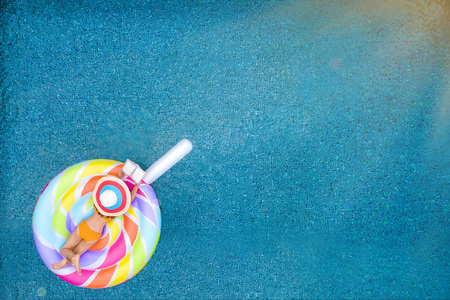 woman in bikini enjoy playing tablet on line in candy toffee floating tube in middle of swimming...