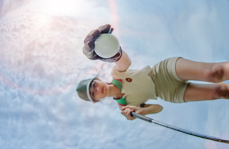 low and bottom view of golf ball in hand of young woman player taking from hole ground of the green with sky in backgroundの写真素材