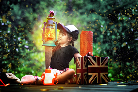 a little girl holding lamp light sitting on the wooden bridge in the forest of fen marsh, see bundle of firefly in early dark of the night, field trip for a kids school learning the nature experienceの写真素材