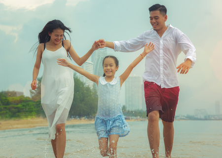 Happy asian family - father, mother, kid hold hands and run together with fun along daylight sea beach. Travel, active lifestyle, parents with children on tropical summer vacations.の写真素材