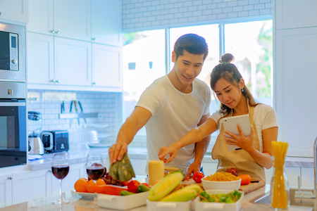 couple lover help on each other cooking online, learning cooking from website internet for a new married couple home, romantic sweet homeの写真素材