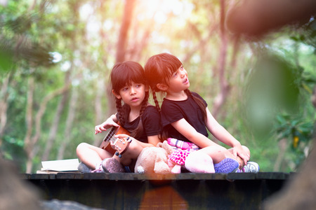 a little twin girls playing ukulele and sing a song together in forest park in holidaysの写真素材