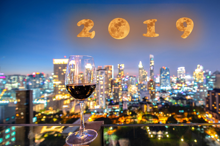 invitation on incoming year 2019 by glass of wine standing for celebration at night with the light bokeh of city shining in background, moon creat in concept celebration of 2019 in backgroundの写真素材
