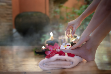 Closeup of hand female holding oil glass salon on feet pedicure procedure. Female legs on decoration the flowers towels, relax and feel comfortable zone spa therapy and treatmentの写真素材