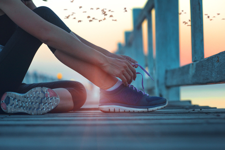 hand of woman sport runner sitting on the sea wooden bridge tie shoelack after jog along the suset, tie lace shoe after long jogging exerciseの写真素材