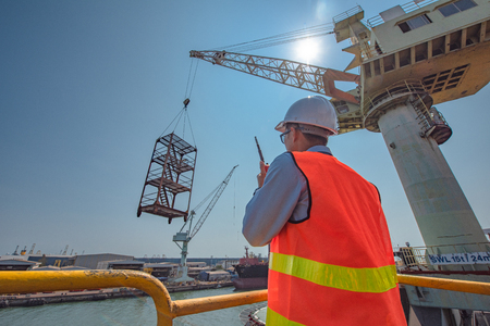 stevedore or foreman, engineering, loading master talks to crane driver by walkie talkie for safety lifting  the goods shipment, lifting by gantry crane, working at risk on the high level insuranceの写真素材