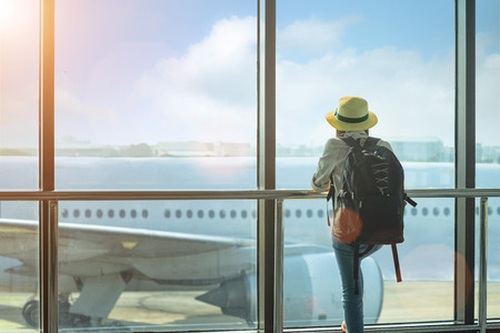 woman passenger traveler or tourist looking at the aircraft just leaving from the terminal, holding...