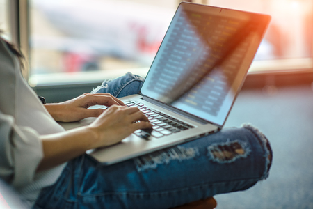 Hand of woman traveller typing on keyboard of computor in transit area of airport, stand by for the next schedule traveling, late delay of the arrival departure, missing checking in timeの写真素材