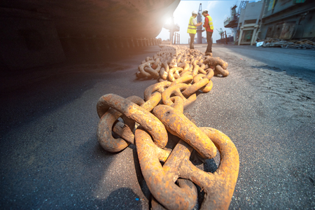 anchor chains bundle laying at bottom layer of the ship in floating dry dock terminal, for recondition maintennance with sand blasting perform, port control and inspector surveying condition in backgroundの写真素材