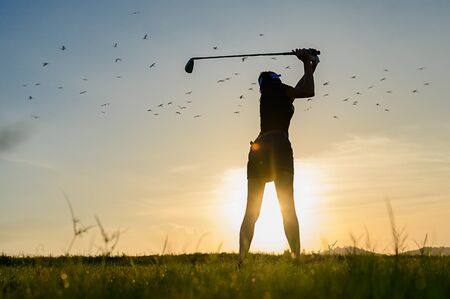 silhouette woman golfer going to hit the golf ball on the fairway at sunsetの写真素材