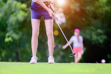 young woman golf player holding putter to hit golf ball to the destination of golf hole on the...