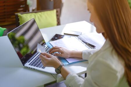 hand of woman hold notebook keyboard going to pay goods online by credit card, working woman or freelance in coffee shopの写真素材