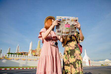 young tourist women holding mapguide with talking discussion find location visit on the palace temple in Bangkok of Thailand, Emerald Buddha Temple, Wat Phra Kaew, Bangkok Royal Palace popular tourist placeの写真素材