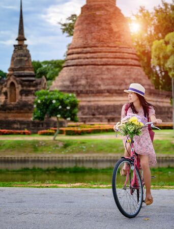 woman tourist enjoy riding vintage bicycle to see the historic park of Thailand, exciting to explore the wonderful place of sightseeingの写真素材