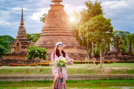 woman tourist enjoy riding vintage bicycle to see the historic park of Thailand, resting or closed eye to recall an incarnation of history to explore the wonderful place of sightseeingの写真素材