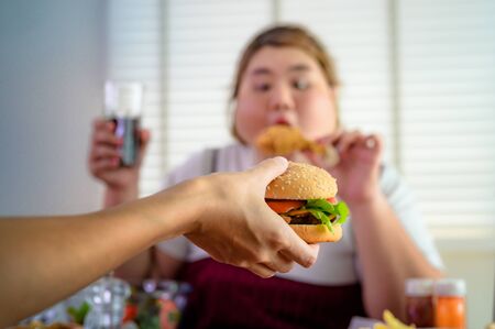 hamburger being serv to woman hunger in background, junk food eating a lot by fatty womanの写真素材