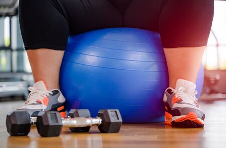 fat plump woman playing around with gym ball exercise, sitting or resting on the ballの写真素材