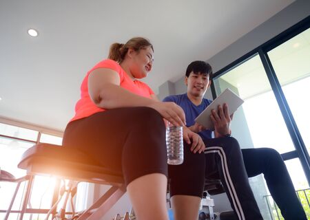 fat plump woman learning health report from the exercise record in device with suggestion by personal trainer or coachの写真素材