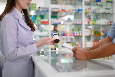 bottle of medicine tablets or pills in hand of woman pharmacist in explanation apply to man...