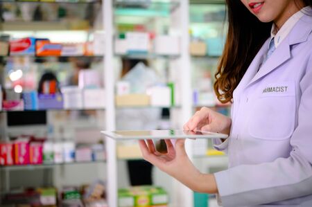 hand of woman pharmacist checking inventory list of medicine remaining or balance in stock, working on line device list of stockの写真素材
