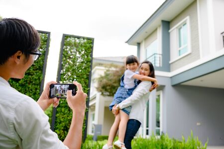hand of father holding mobile device taking picture family with dreaming home, new family meeting new home buyingの写真素材