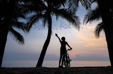 silhouette of woman riding bicycle along the sea beach at sunset, cheerfully at the end of the dayの写真素材