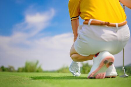 hand of woman golfer holding golf ball to marking point to being putting on the green of golf courseの写真素材