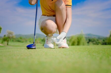 Hand of woman golfer laying golf ball onto wooden tee on tee off pin on the golf course, ready to hit ball away to the fairwayの写真素材