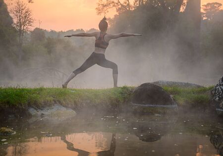 young woman in action of yoga practice in steaming hot spring water, the nature yoga exercise in hot spring steaming water at morning sunrise の写真素材