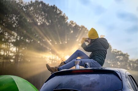 Woman traveller enjoy coffee time and make selfie on her owns roof of the car with scenery view of the mountain and mist morning in backgroundの写真素材