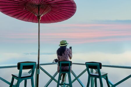 woman traveller relax sitting on the terrace enjoy takes photo of mist and foggy morning, Mae Hong...