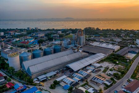 feed mill factory in production line at sunset and sea view in back ground, factory produce line of industrial estate area locate in middle of the city town against air pollutionの写真素材