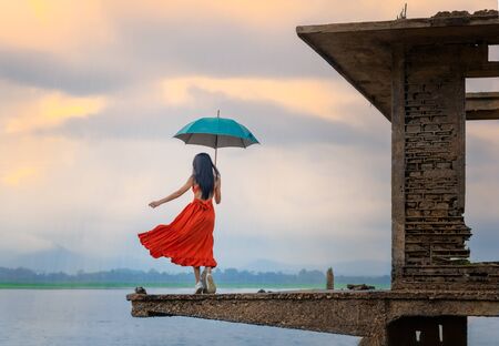 woman fashion dress standsing on the retro old cottage house in the lake, holding umbrella under raining seasonの写真素材