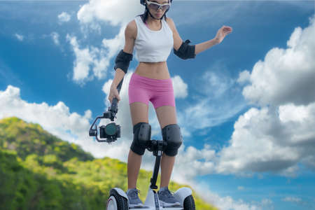 woman sporty riding scooter upon the hill holding gimbal camera to takes VDO capture moving object