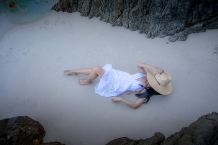 Woman tourist in white dress laying down on the sand of the sea, relax moment of the woman iat the edge of the sea beach in summer courseの写真素材