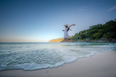 Woman tourist in white dress play around jumping on the sand of the sea, rejoy moment of the woman at the edge of the sea beach in summer courseの写真素材
