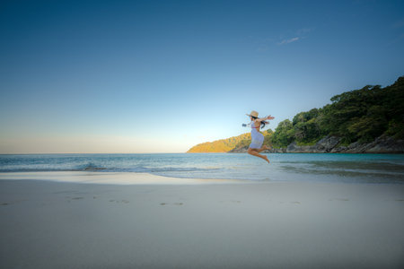 Woman tourist in white dress play around jumping on the sand of the sea, rejoy moment of the woman at the edge of the sea beach in summer courseの写真素材
