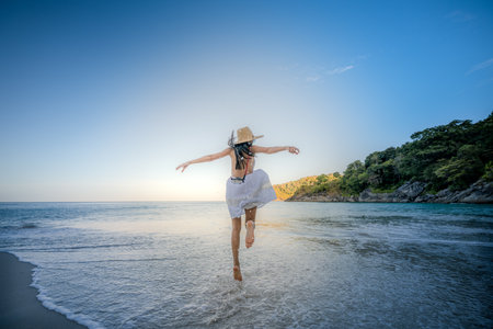 Woman tourist in white dress play around jumping on the sand of the sea, rejoy moment of the woman at the edge of the sea beach in summer courseの写真素材