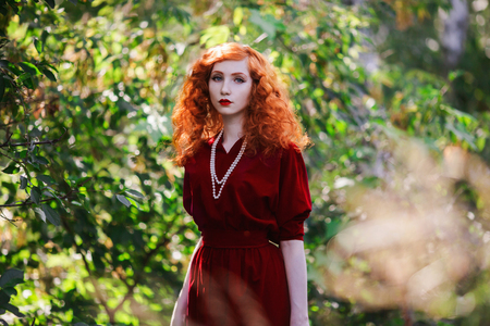 Woman With Red Hair And Red Dress Posing On A Background Of Green