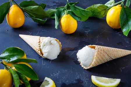 lemon ice-cream in waffle cone on a dark background. Side view. Lemons on a branch with green...