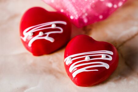 cakes in the form of glazed red hearts on a pink marble table, close-up.の写真素材