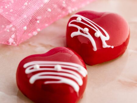 cakes in the form of glazed red hearts on a pink marble table, close-up.の写真素材