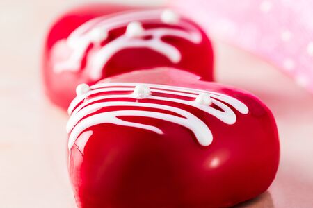 cakes in the form of glazed red hearts on a pink marble table, close-up.の写真素材