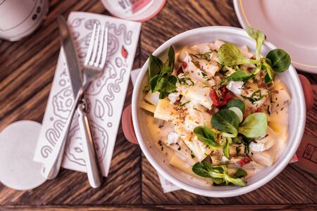 pasta with sauce, cheese and basil in a white dish on a wooden table in a restaurant, a rowl knife...