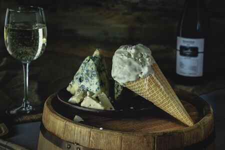 gorgonzola ice cream in a cone on a wooden table, gorgonzola cheese on a clay dish, a glass of wine, a bottle of wine, dark backgroundの写真素材