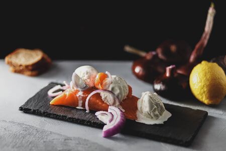 ice cream with sweet onions on a fillet of red fish, stone stand, on a background of lemon, red onionの写真素材